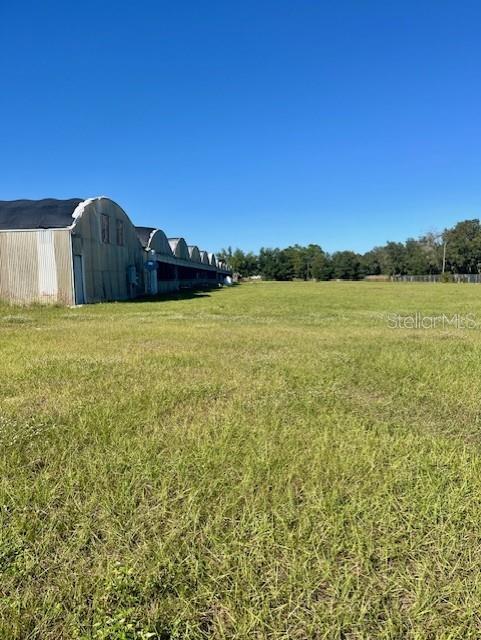 A large, open grassy field sits beside a long row of metal agricultural buildings — 4103 ONDICH ROAD, APOPKA, FL