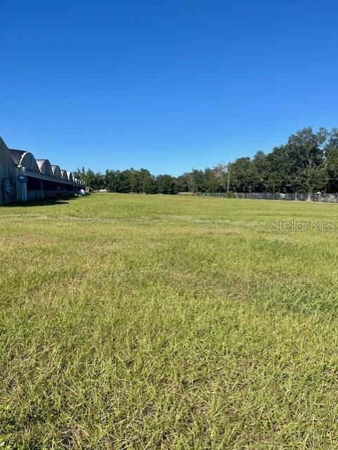 A wide, grassy field sits adjacent to a long, arched agricultural structure under a clear sky — 4103 ONDICH ROAD, APOPKA, FL