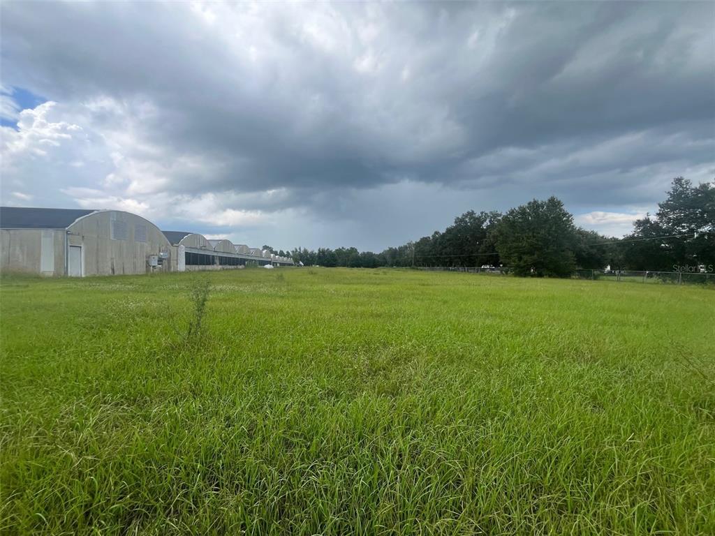 A large, grassy field sits adjacent to a long, industrial-style building under a cloudy sky — 4103 ONDICH ROAD, APOPKA, FL