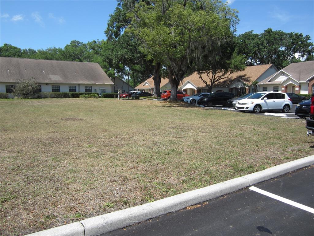 A grassy vacant lot sits in front of a parking area and residential buildings — 209 CRYSTAL GROVE BOULEVARD, LUTZ, FL