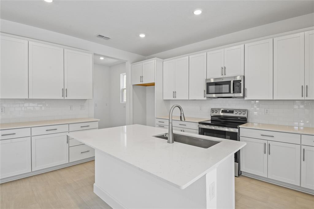 A modern kitchen features white cabinets, a central island with a sink, and stainless appliances — 3716 DEER RIDGE DRIVE, MOUNT DORA, FL