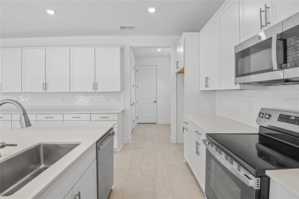 A modern kitchen features white cabinetry, stainless steel appliances, and a central island with sink — 3716 DEER RIDGE DRIVE, MOUNT DORA, FL