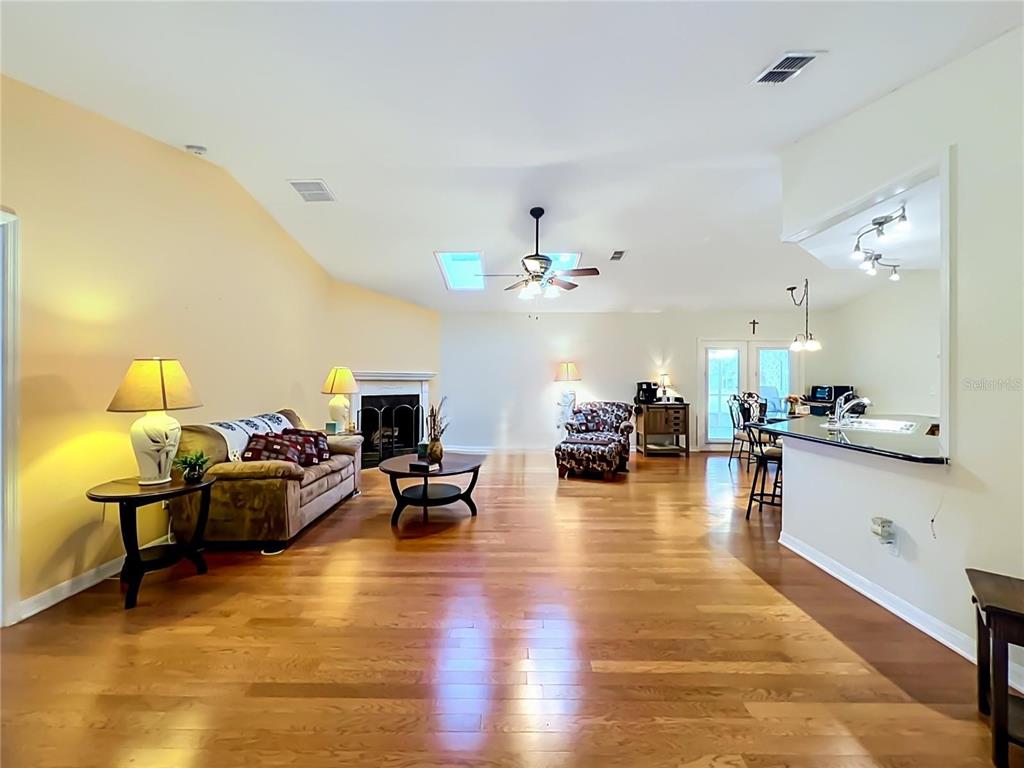 A spacious living room features hardwood floors, a fireplace, a ceiling fan, and an open kitchen — 41821 ROYAL TRAILS ROAD, EUSTIS, FL