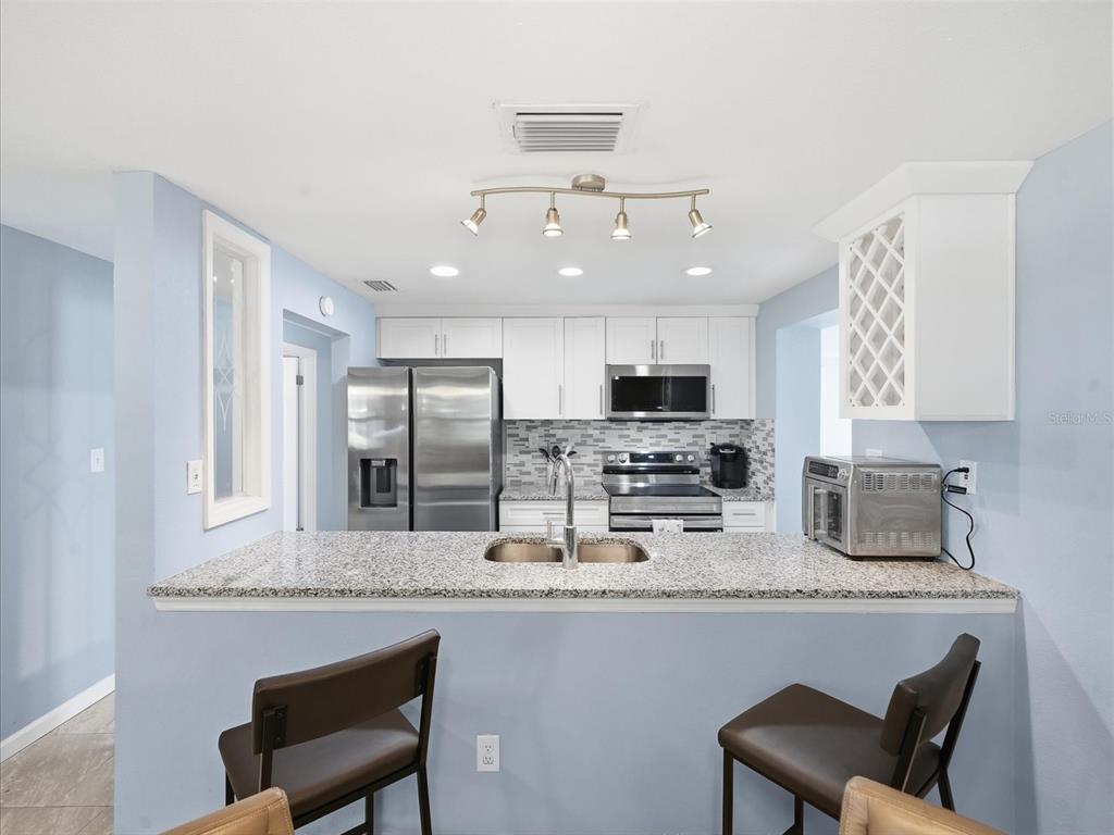 A kitchen with light blue walls, white cabinets, stainless steel appliances, and a granite countertop island — 7312 S ELLIOTT STREET, TAMPA, FL