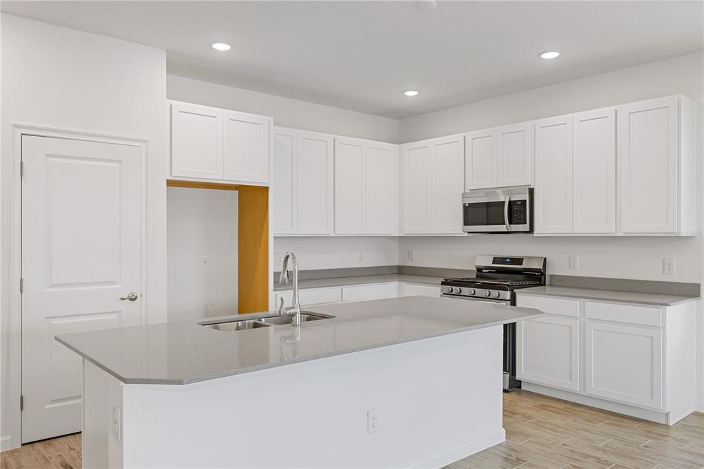 A modern kitchen features white cabinetry, gray countertops, a center island, and stainless steel appliances — 2240 SIRENA LANE, MOUNT DORA, FL
