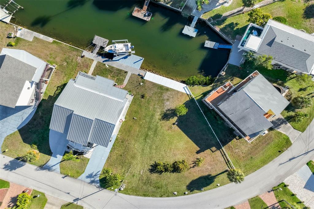 An aerial view shows two waterfront houses with metal roofs and private boat docks — 6424 DRIFTWOOD DRIVE, HUDSON, FL