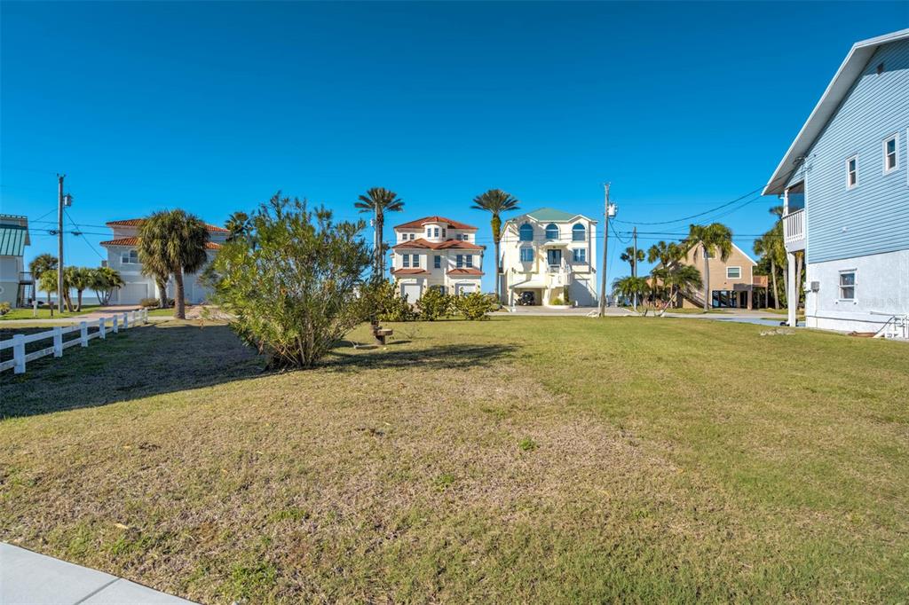 A grassy vacant lot sits in front of several multi-story coastal houses under a clear sky — 6424 DRIFTWOOD DRIVE, HUDSON, FL