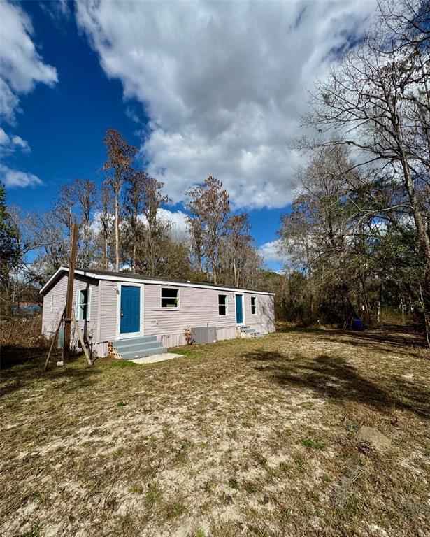A light-colored mobile home sits on a grassy lot surrounded by bare trees — 26931 DEACON LOOP, ZEPHYRHILLS, FL