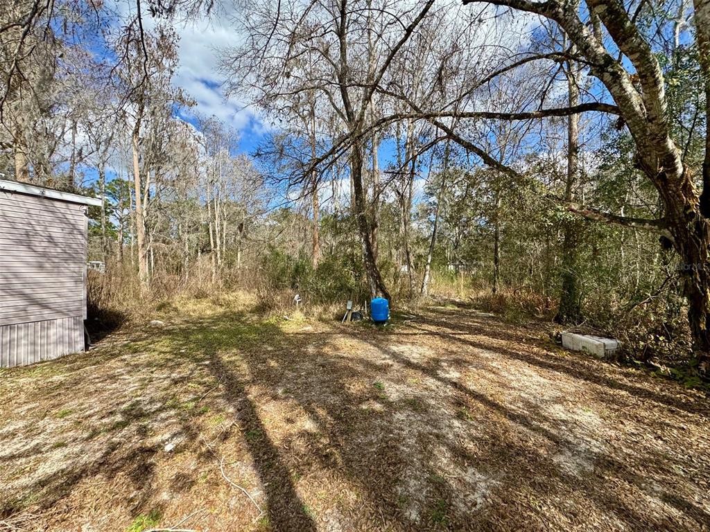 A view of a sandy yard next to a mobile home with a blue water tank — 26931 DEACON LOOP, ZEPHYRHILLS, FL
