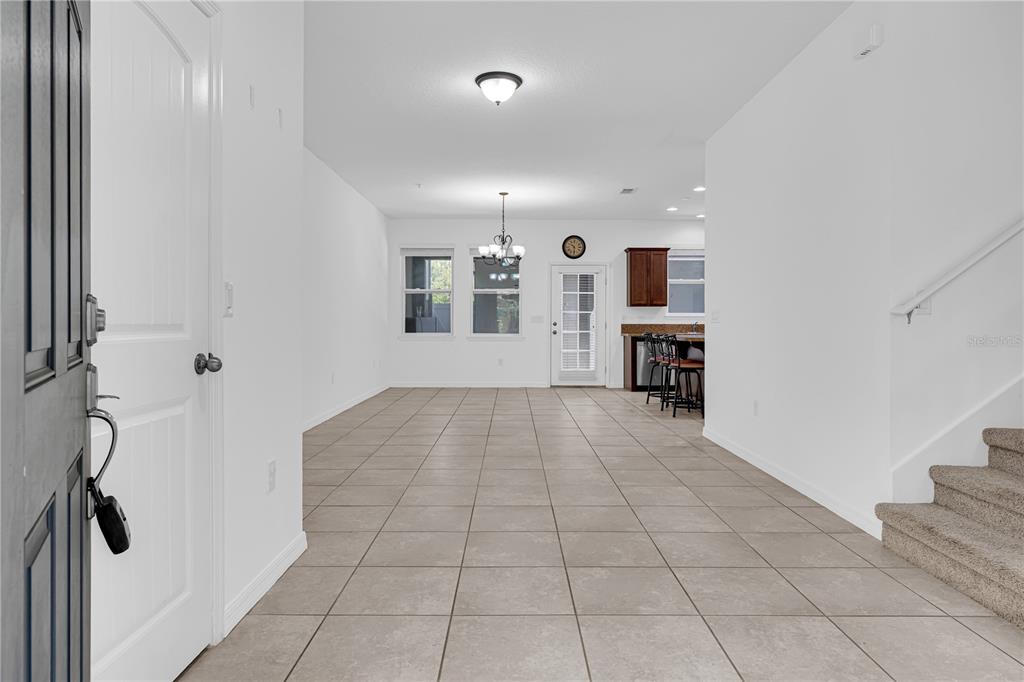 An open-concept living area features tile flooring, white walls, a staircase, and a kitchen — 4450 CAPITAL BOULEVARD, ST CLOUD, FL
