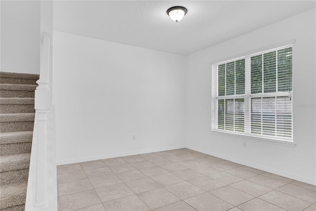 A room with white walls, tile flooring, a window with blinds, and a carpeted staircase — 4450 CAPITAL BOULEVARD, ST CLOUD, FL