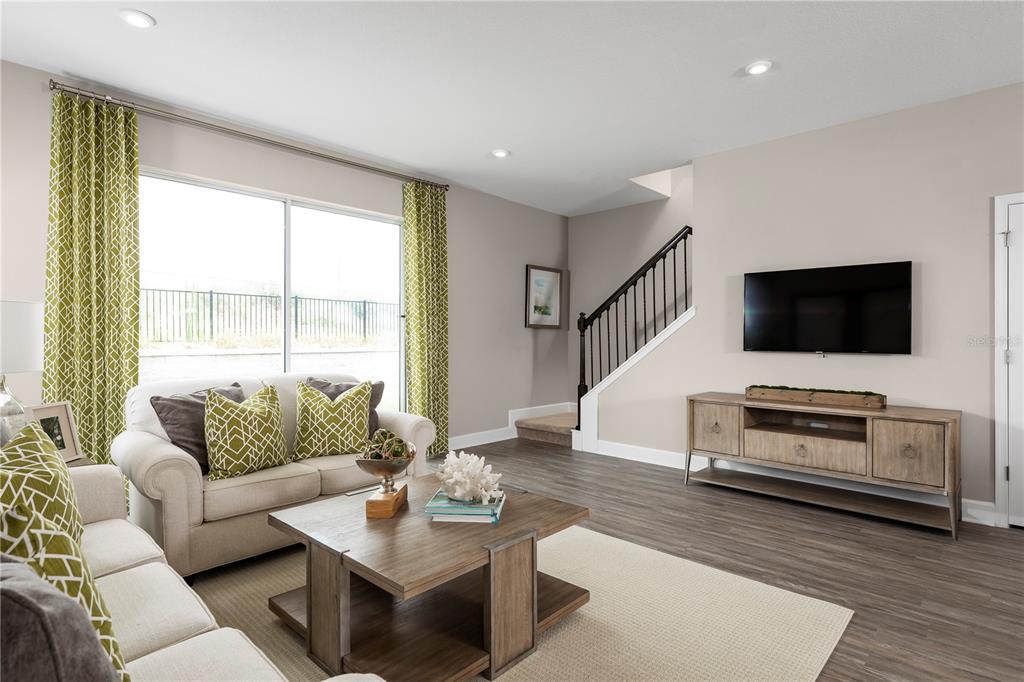 A living room features a beige sofa, wooden coffee table, media console, and a staircase — 6692 CEDAR LANDING CIRCLE, LEESBURG, FL