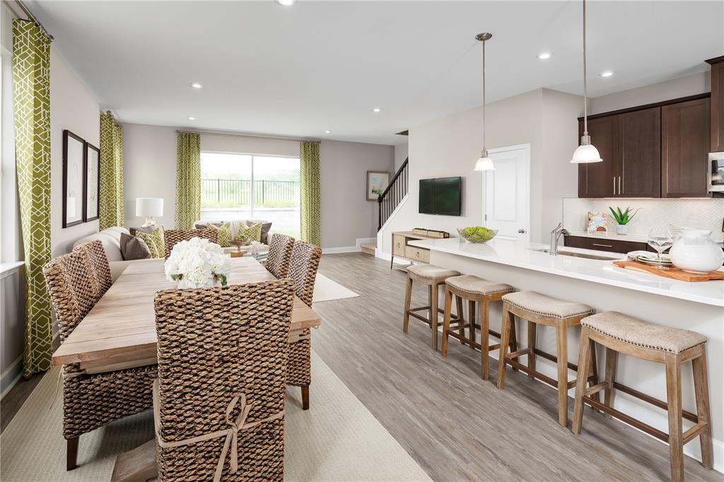 An open-concept kitchen and dining area features woven chairs, a white island, and wood flooring — 6692 CEDAR LANDING CIRCLE, LEESBURG, FL