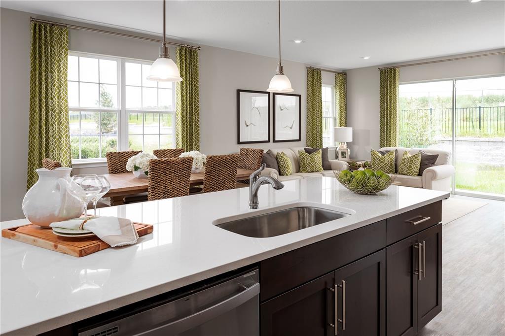 A kitchen island with a stainless steel sink overlooks an open-concept dining and living area — 6692 CEDAR LANDING CIRCLE, LEESBURG, FL