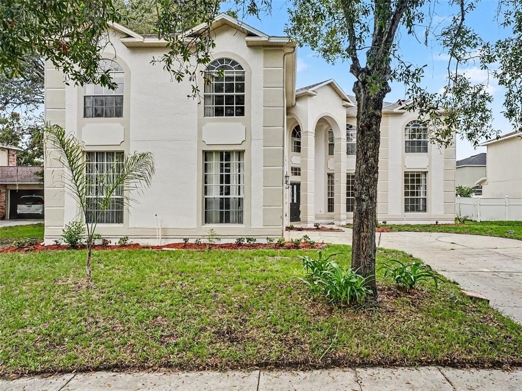 A two-story stucco house with arched windows and a paved driveway under a blue sky — 1268 FOXFORREST CIRCLE, APOPKA, FL