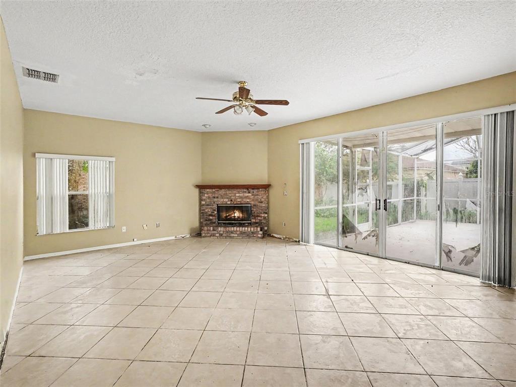 A spacious living room features beige tile floors, a brick fireplace, and sliding glass patio doors — 1268 FOXFORREST CIRCLE, APOPKA, FL