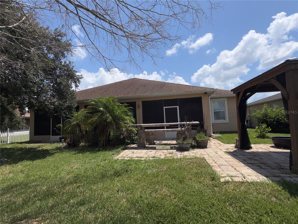 A backyard view featuring a screened-in porch, a stone patio, and a wooden pergola — 3212 MERRICK AVENUE, ROCKLEDGE, FL