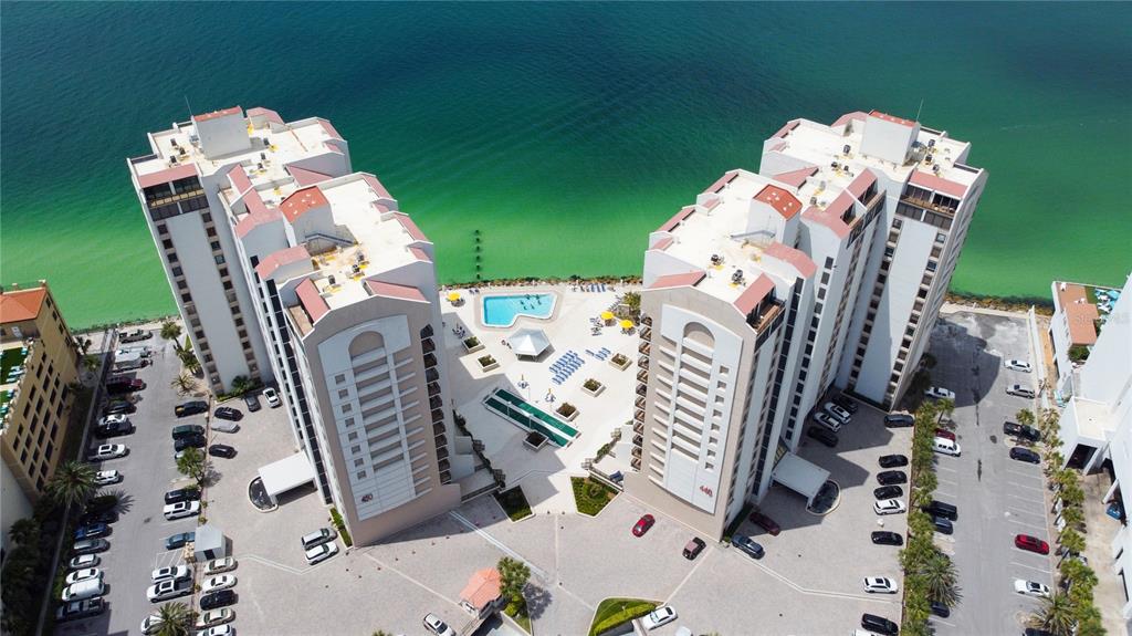 An aerial view shows two tall apartment buildings with a shared pool area by the water — 440 S GULFVIEW BOULEVARD UNIT 1002, CLEARWATER BEACH, FL