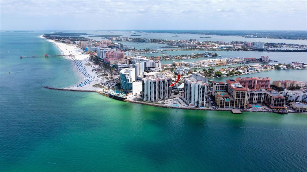 An aerial view shows a high-rise condominium building on a beach with a red arrow — 440 S GULFVIEW BOULEVARD UNIT 1002, CLEARWATER BEACH, FL