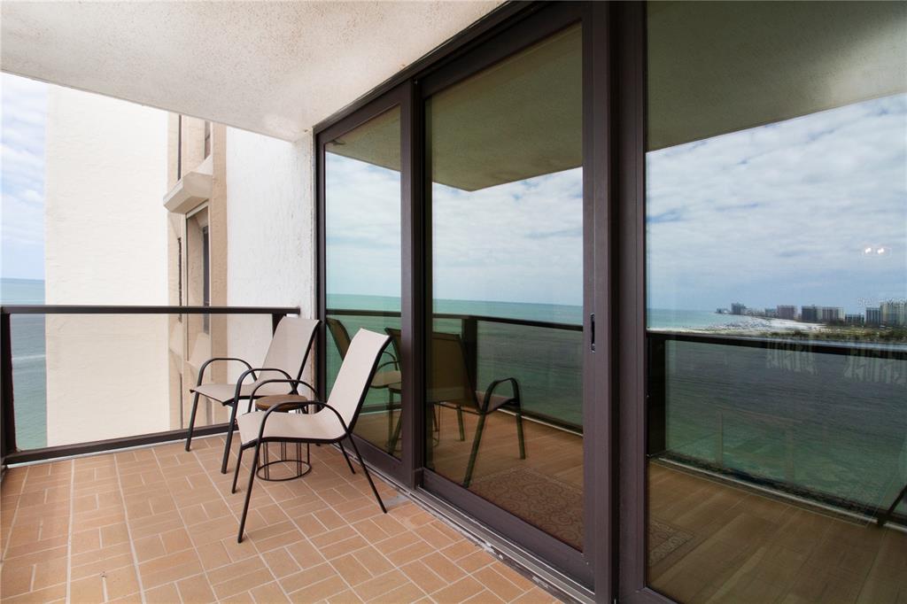 A balcony with two chairs overlooks the ocean through large sliding glass doors — 440 S GULFVIEW BOULEVARD UNIT 1002, CLEARWATER BEACH, FL