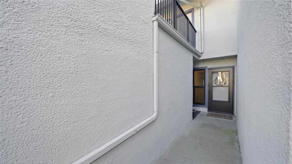 A concrete walkway leads to a dark-framed glass door between two textured white walls — 890 A1A BEACH BOULEVARD UNIT 31, ST AUGUSTINE, FL