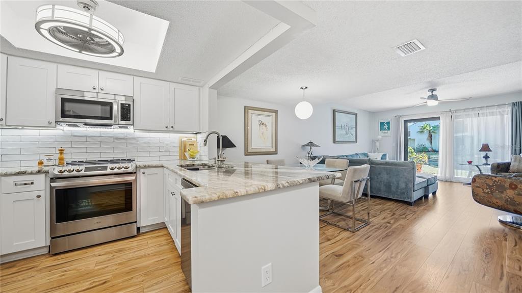 A kitchen with white cabinets and granite countertops opens into a living room with wood flooring — 890 A1A BEACH BOULEVARD UNIT 31, ST AUGUSTINE, FL