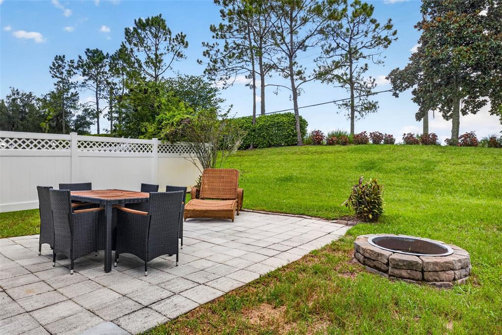 A paved patio features a dining set, a lounge chair, and a stone fire pit — 7360 BRIDGEVIEW, WESLEY CHAPEL, FL