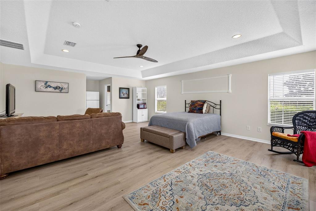 A spacious bedroom features light wood-look flooring, a tray ceiling, a bed, and a sofa — 7360 BRIDGEVIEW, WESLEY CHAPEL, FL