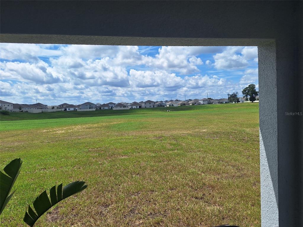 A view of a large grassy field and distant houses from a covered patio — 4728 SW 85TH PLACE, OCALA, FL