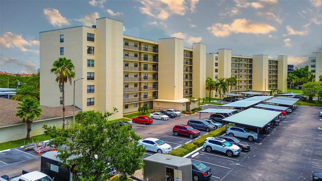 An exterior view of a multi-story apartment building with a parking lot and covered carports — 1000 COVE CAY DRIVE UNIT 2C, CLEARWATER, FL