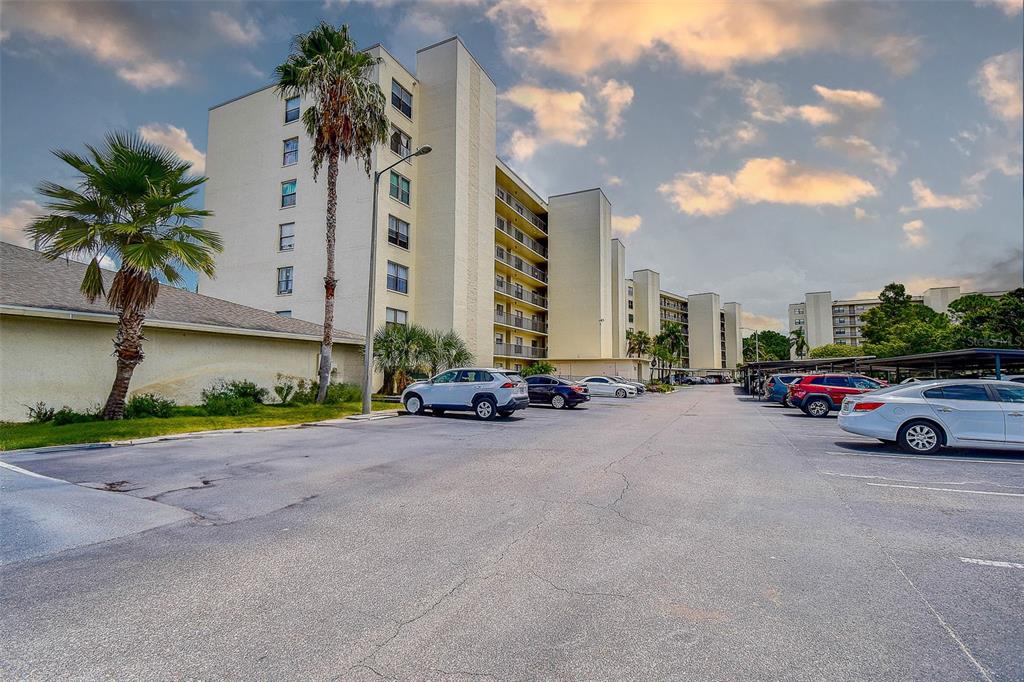 A multi-story apartment building with a parking lot and palm trees under a cloudy sky — 1000 COVE CAY DRIVE UNIT 2C, CLEARWATER, FL