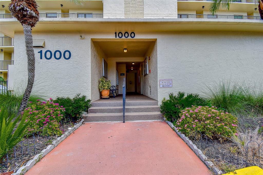 The exterior entrance of a multi-story apartment building features a concrete walkway and steps — 1000 COVE CAY DRIVE UNIT 2C, CLEARWATER, FL