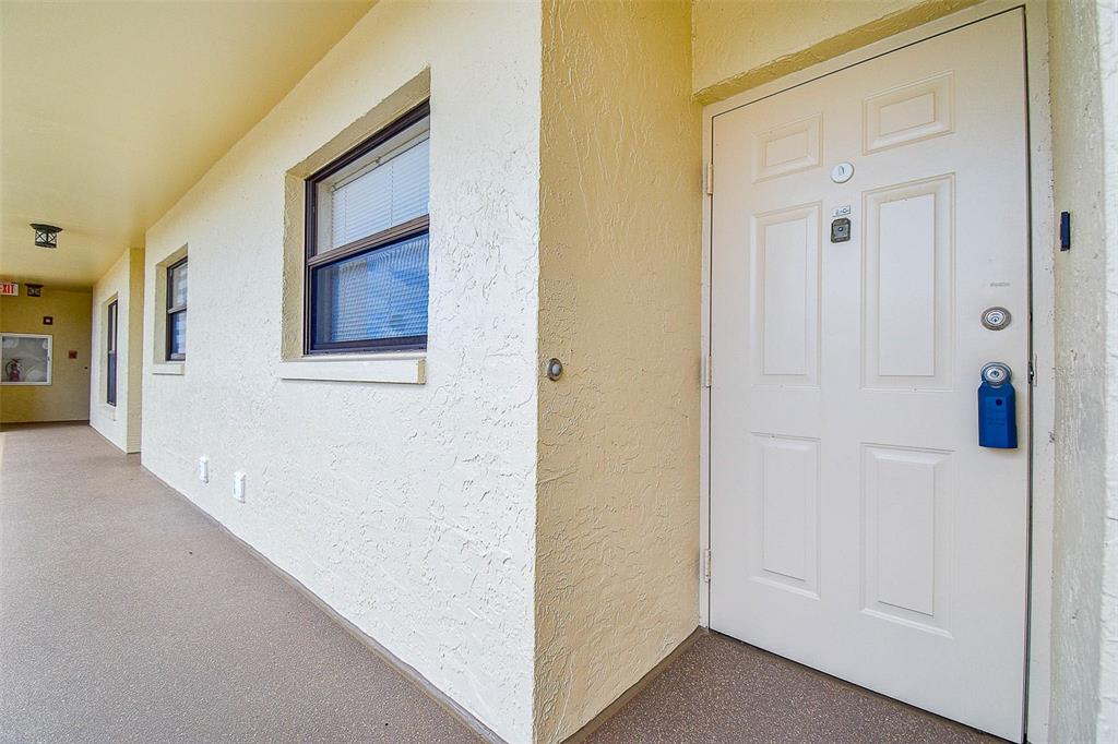 A white front door with a blue lockbox sits on a covered outdoor apartment walkway — 1000 COVE CAY DRIVE UNIT 2C, CLEARWATER, FL