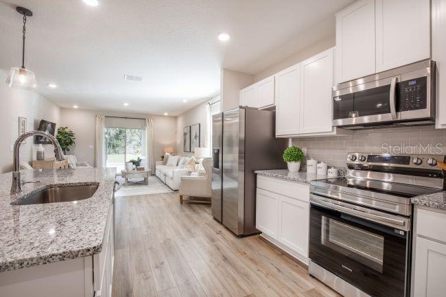 A kitchen with granite countertops and stainless steel appliances opens into a living room — 31400 MALBEC DRIVE, BROOKSVILLE, FL