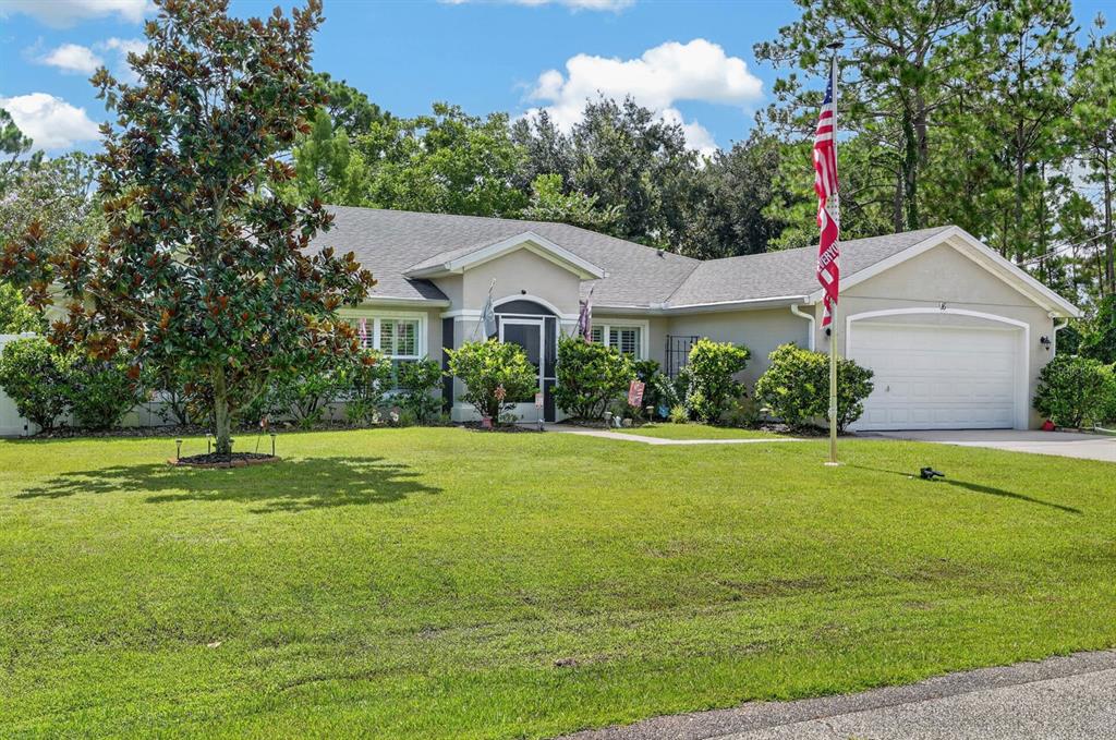 A single-story house with a beige exterior, a two-car garage, and a large front lawn — 16 SEVEN CHAMPIONS PATH N, PALM COAST, FL