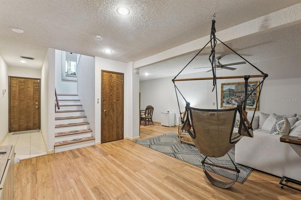 A living room features wood-look flooring, a hanging chair, stairs, and a sectional sofa — 308 N GARFIELD AVENUE, DELAND, FL