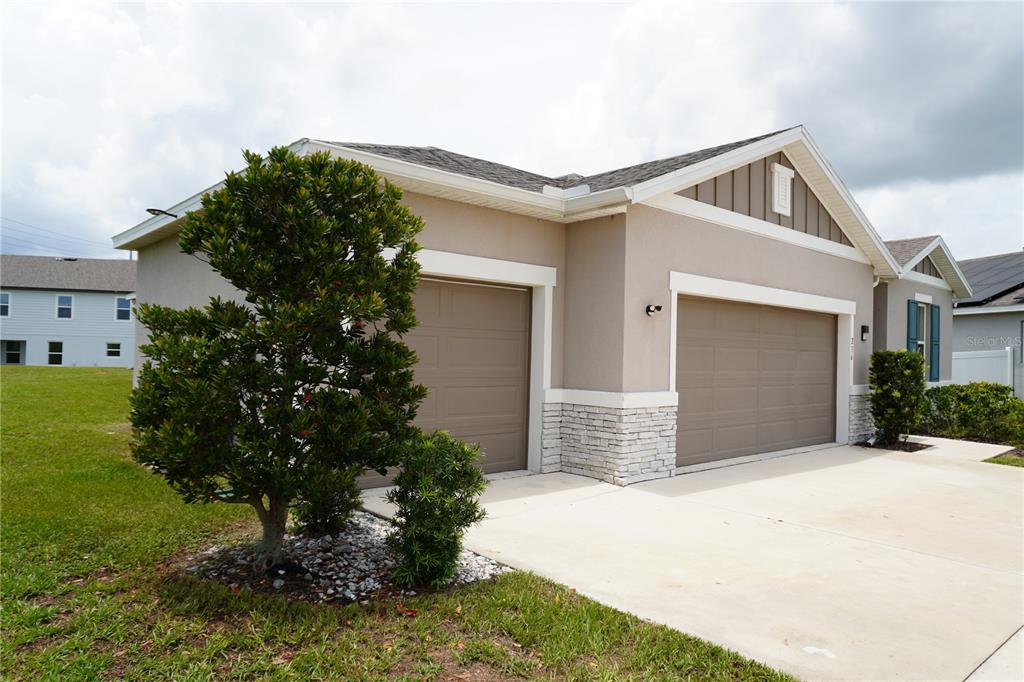 A tan single-story house with a three-car garage and stone accents under a cloudy sky — 236 HILLCREST DRIVE, DUNDEE, FL