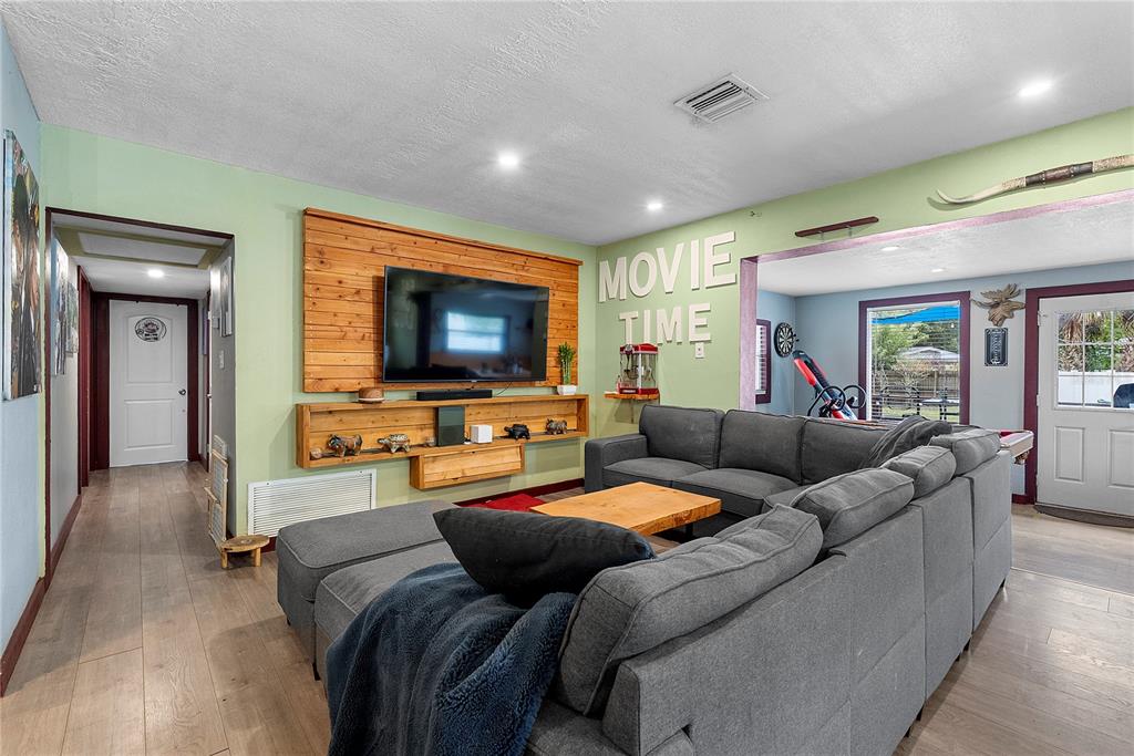 A living room features a large gray sectional sofa, a wood-paneled accent wall, and light flooring — 1428 MAURY ROAD, ORLANDO, FL