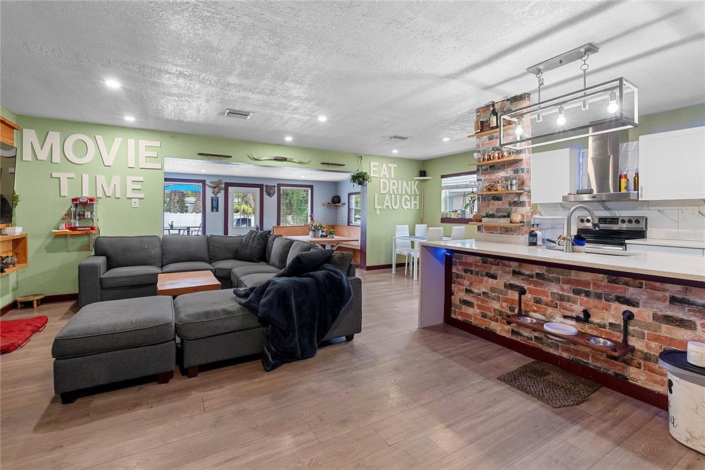 An open-concept living room and kitchen feature a brick island, gray sectional, and green walls — 1428 MAURY ROAD, ORLANDO, FL