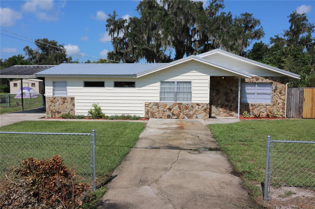 A single-story house with light siding and stone accents sits behind a chain-link fence — 2620 HOWARD STREET, MULBERRY, FL