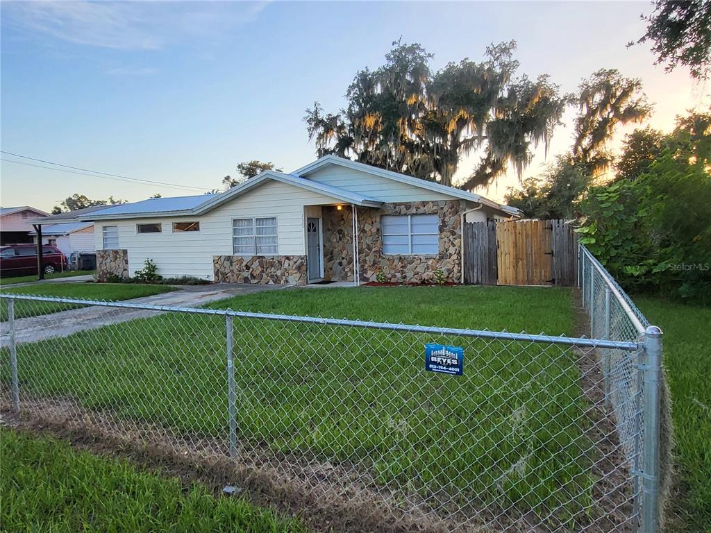 A single-story house with light siding and stone accents sits behind a chain-link fence — 2620 HOWARD STREET, MULBERRY, FL