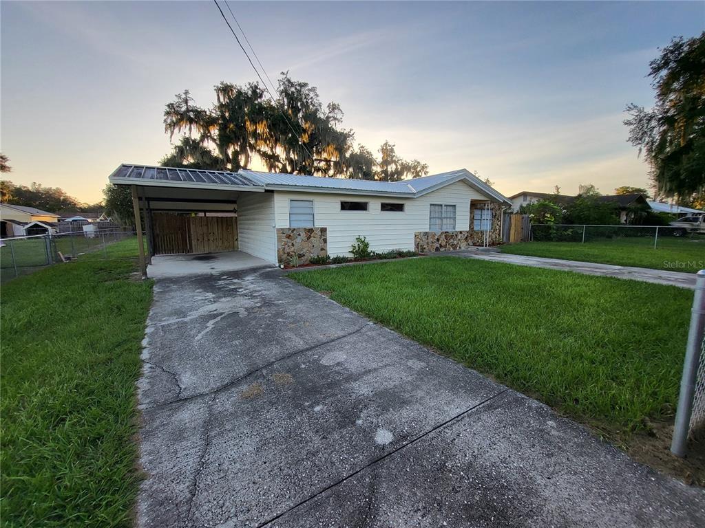 A single-story house with a carport, stone accents, and a concrete driveway under a sunset — 2620 HOWARD STREET, MULBERRY, FL