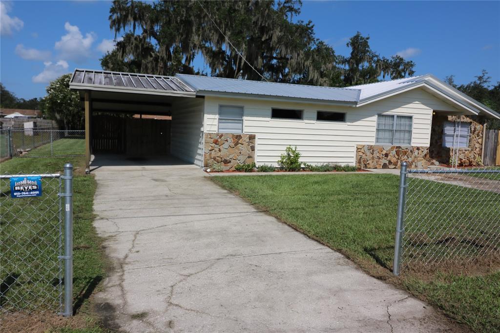 A single-story house with light siding, stone accents, and a metal carport under a sunset sky — 2620 HOWARD STREET, MULBERRY, FL