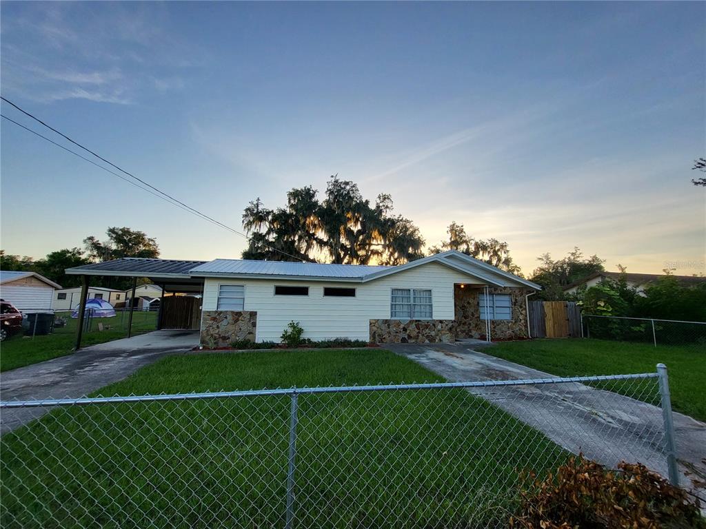 A single-story house with light siding, stone accents, and a metal carport under a sunset sky — 2620 HOWARD STREET, MULBERRY, FL