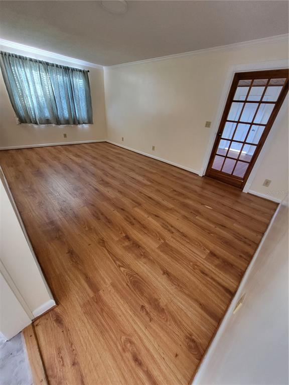 An empty room features wood-look flooring, cream-colored walls, a window with curtains, and a French door — 2620 HOWARD STREET, MULBERRY, FL