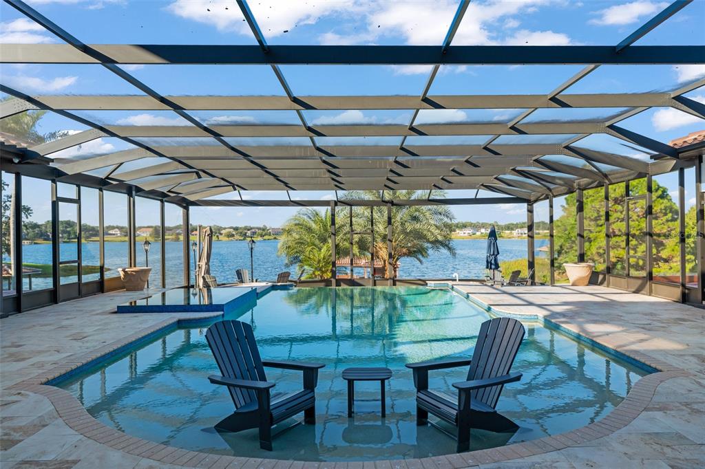 A screened-in pool patio features two chairs in the water overlooking a lake — 9575 WESTOVER ROBERTS ROAD, WINDERMERE, FL