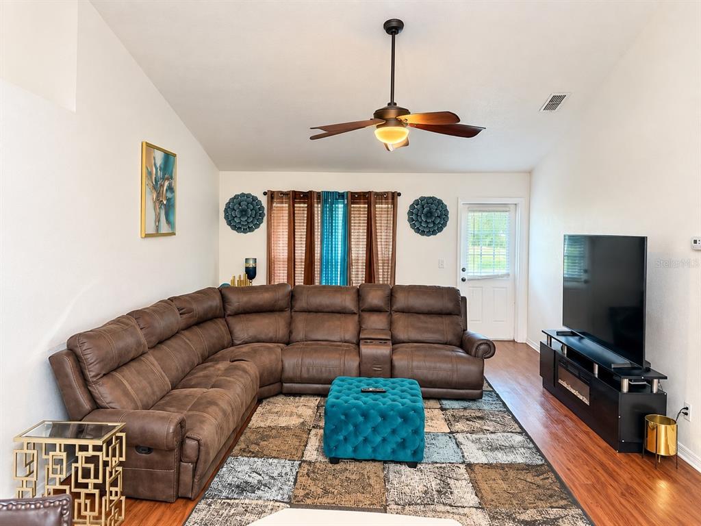 A living room features a brown sectional sofa, a teal ottoman, and a television console — 24107 MILFORD DRIVE, EUSTIS, FL