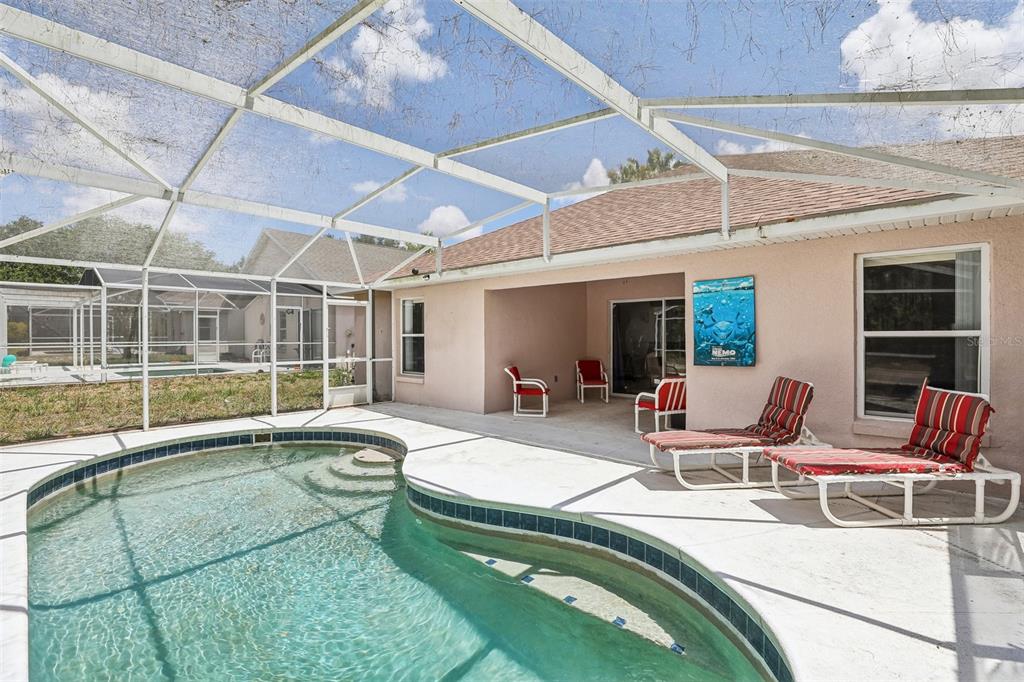 A swimming pool with a screened enclosure sits on a patio behind a peach-colored house — 536 PINE CONE DRIVE, DAVENPORT, FL