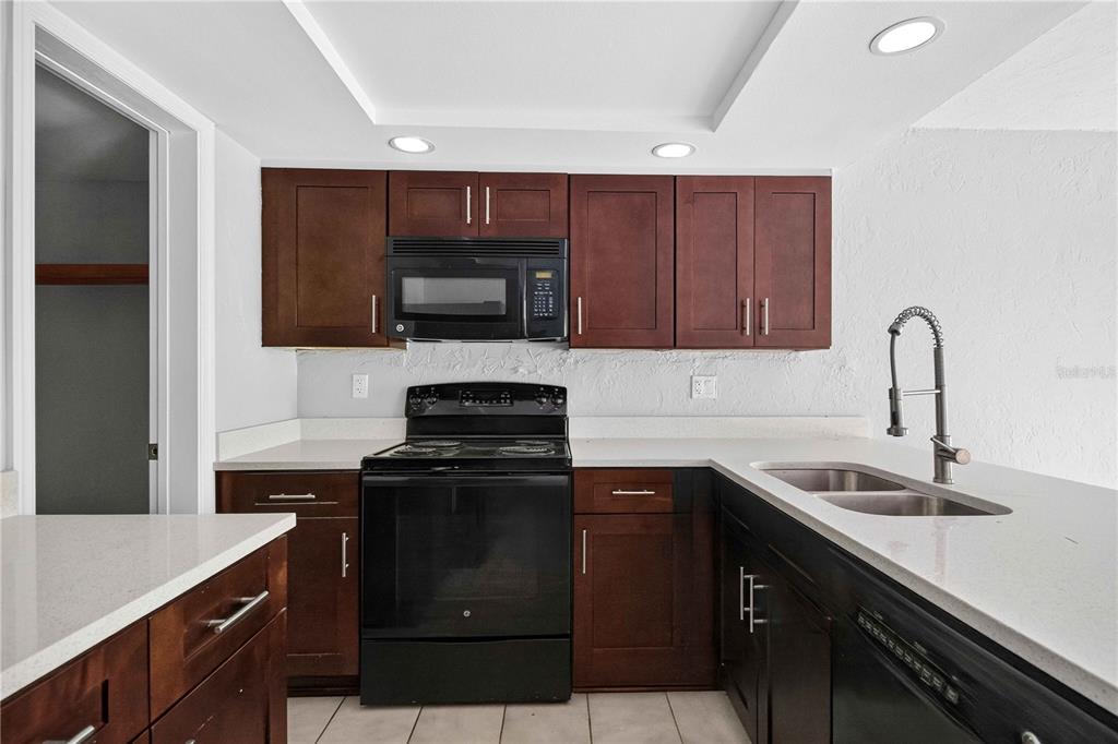 A kitchen features dark wood cabinets, black appliances, and white countertops with a double sink — 1125 LONGFELLOW WAY UNIT 125-B, SARASOTA, FL