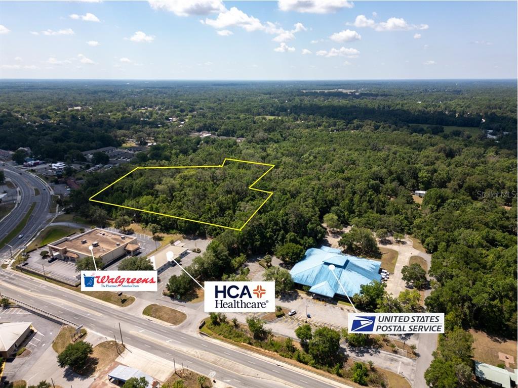 An aerial view shows a wooded lot outlined in yellow near commercial buildings and roads — 11144 SE 55TH AVENUE ROAD, BELLEVIEW, FL